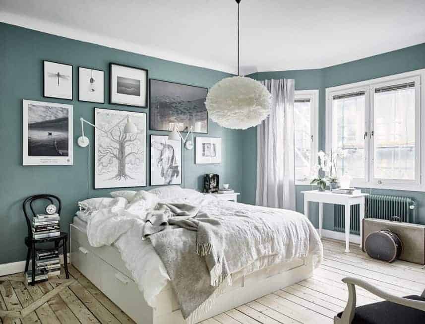 A very attractive Scandinavian-Style primary bedroom with green walls decorated with multiple artistic wall decors. The ceiling lighting looks so charming as well.