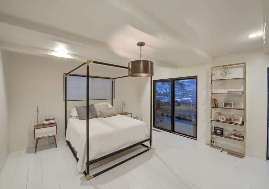 A modish Scandinavian-Style primary bedroom featuring white hardwood floors and stylish side tables along with shelving on the side.