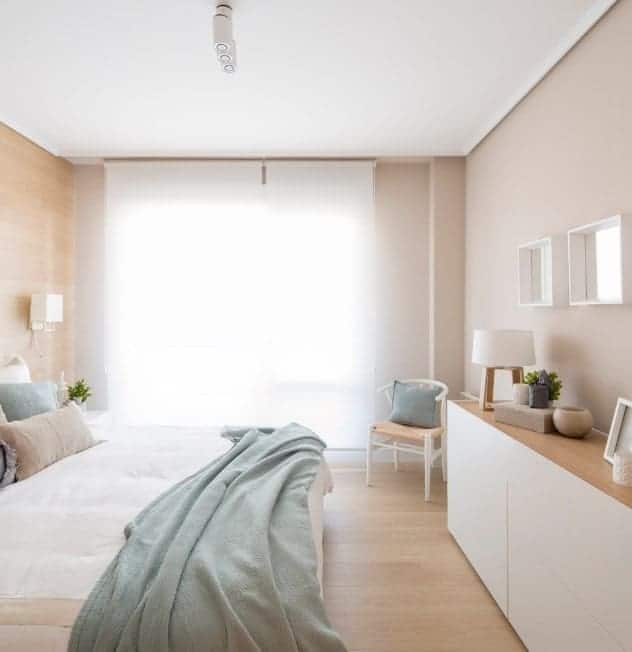 Small Scandinavian-Style primary bedroom with lovely window curtains and beige walls that fit perfectly well with the roomโs style.
