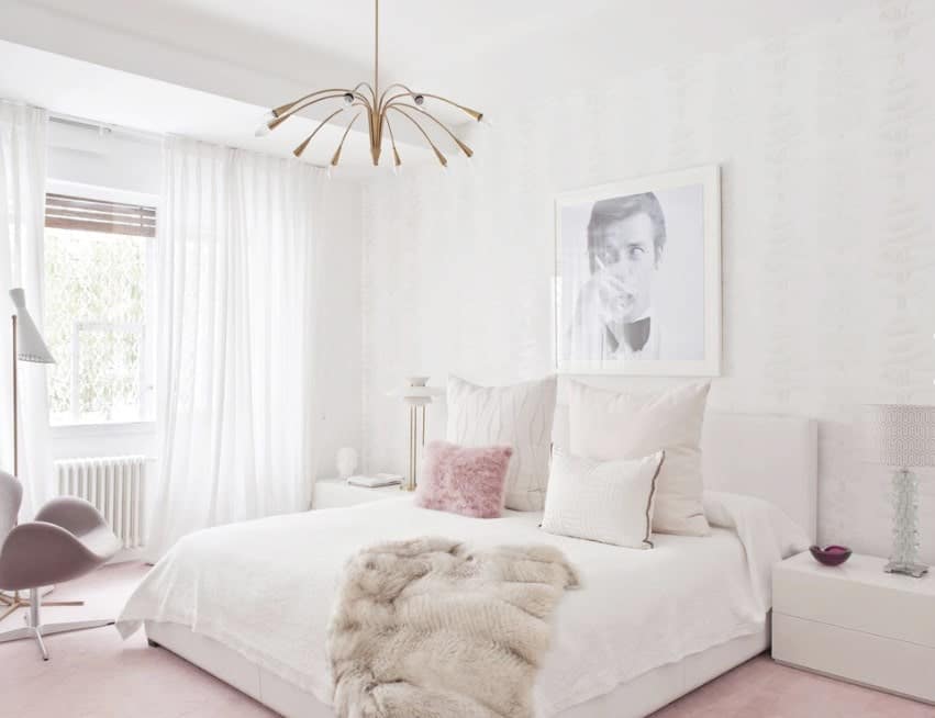A chic Scandinavian-style primary bedroom with pink carpet flooring and white walls that match the bed and side tables perfectly. The white window curtains look very lovely as well.