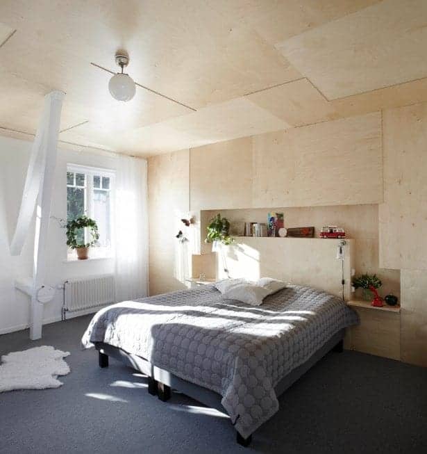This Scandinavian-Style primary bedroom boasts stylish gray carpet flooring and a wooden wall matching the wooden ceiling.