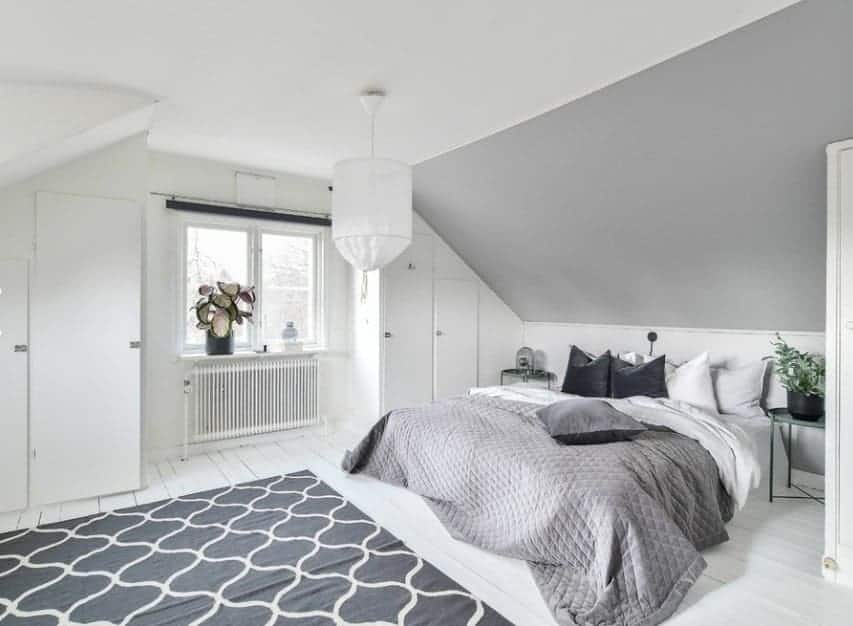 This Scandinavian-Style primary bedroom boasts white walls and ceiling along with white hardwood flooring topped by a stylish rug.