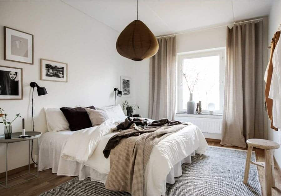 A Scandinavian-Style primary bedroom featuring white walls with multiple eye-catching wall decors on frames. The pendant lighting is very attractive as well.