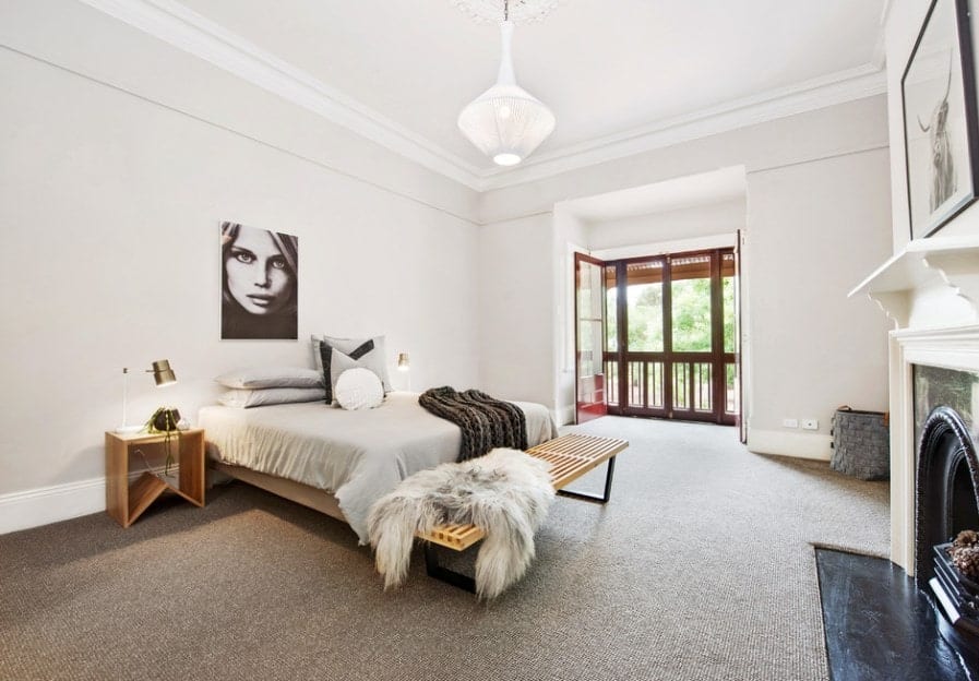Large Scandinavian-Style primary bedroom with white walls and gray carpet flooring along with a classy fireplace.