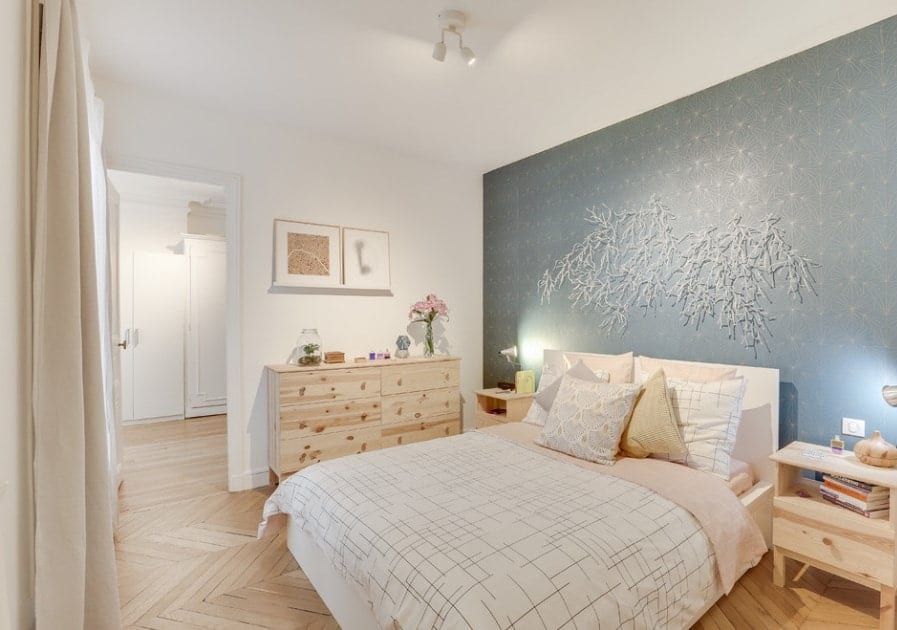 A Scandinavian-Style primary bedroom featuring a very stylish wall with bright and cute decorations along with the roomโs charming herringbone hardwood flooring.