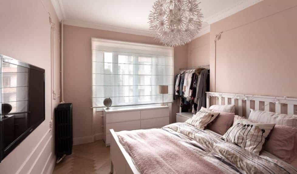 This is a distinctly chic Scandinavian-style room with its pink walls and bedsheets paired with spherical pendant light with dandelion designs. This theme is amplified by the string lights on the wooden headboard of the mission type bed.