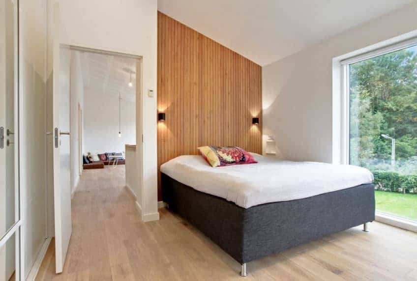 This Scandinavian-style bedroom has a white shed ceiling that tops the lovely alcove where the cushioned platform bed is placed. At the head of the bed is a wall with a wooden shiplap finish that serves as a nice headboard that holds two wall-mounted lamps flanking the bed.