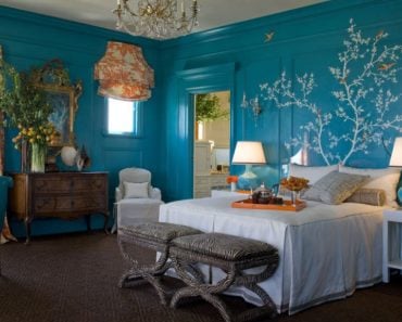 Eclectic blue master bedroom with wall mural, orange draperies and carpet flooring.