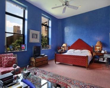 Large Eclectic master bedroom that creates a three-piece visual layers from the shed ceiling, deep blue walls and rustic carpet flooring.