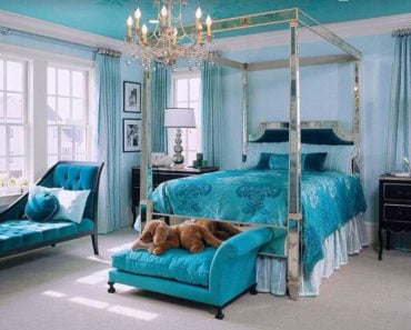 This eclectic master bedroom makes the chandelier and four poster bed frame sparkle against the blue backdrop.