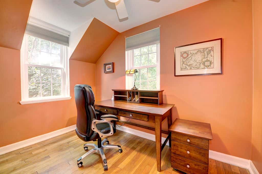 Charming home office furnished with a wooden desk and matching filing cabinet along with black leather office chair.
