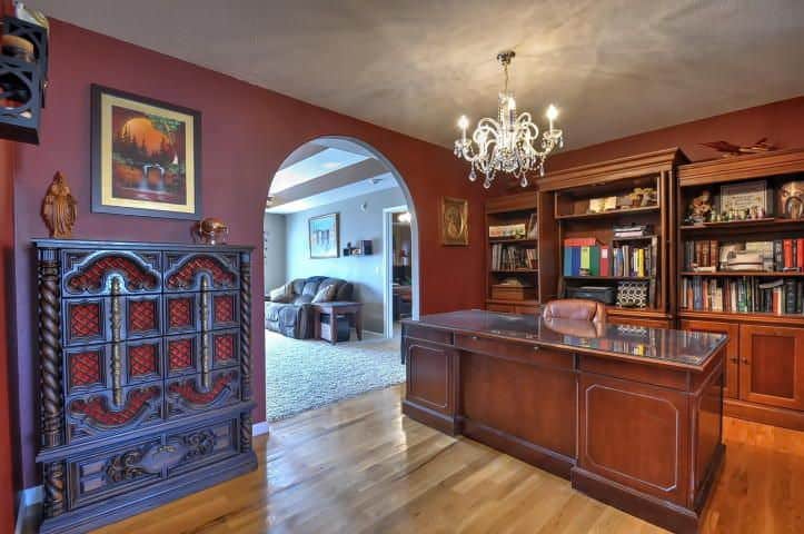 An arched doorway opens to a fabulous living room with a tall ornate console table and wooden office desk illuminated by a fancy chandelier.