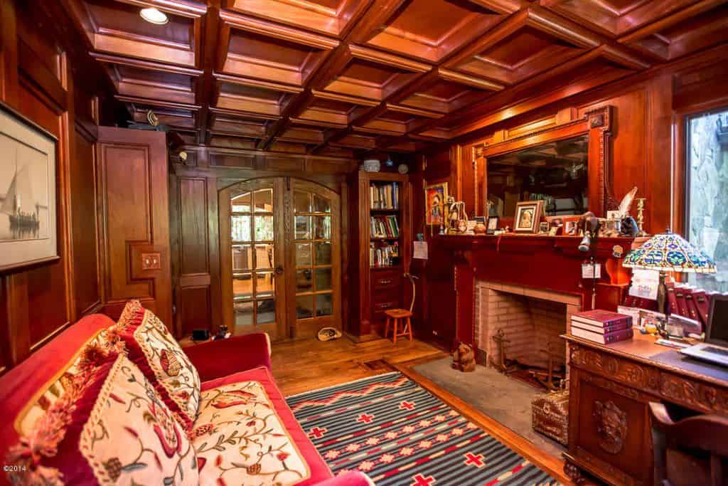 This home office showcases an arched french door and hardwood flooring topped by a lovely striped rug. It has a red floral sofa that faces the fireplace and wood carved desk.