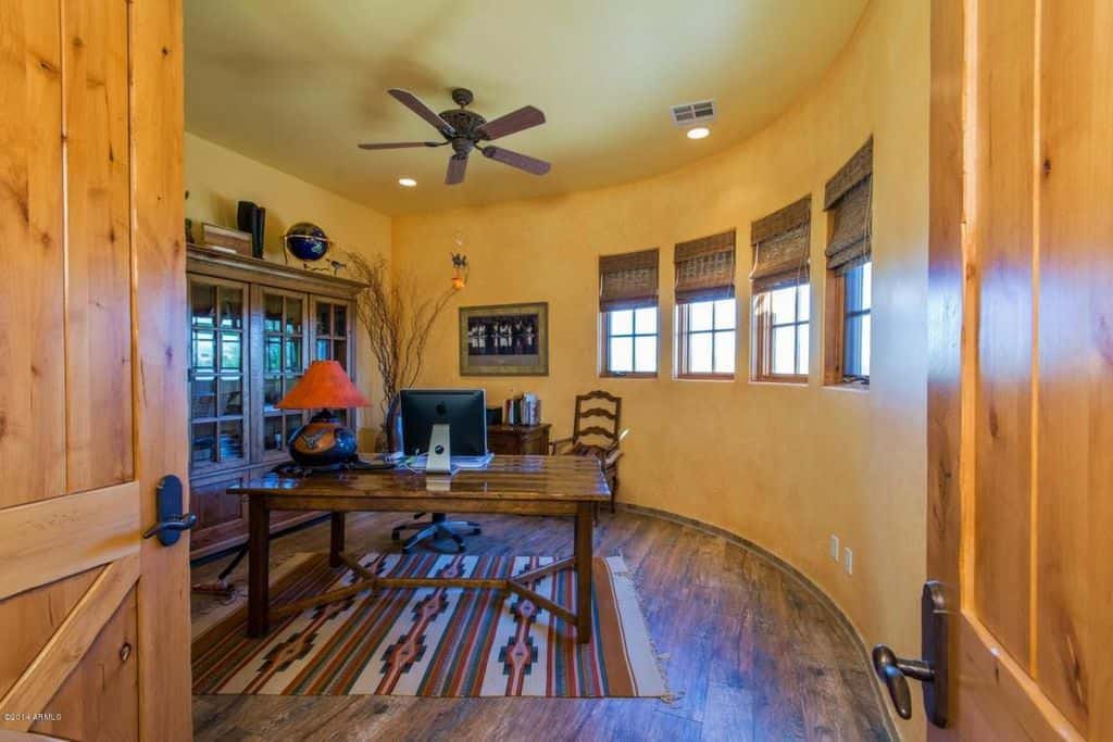 Southwestern home office features yellow walls fitted with a series of glass windows along with a rustic wood plank flooring topped by a tassel rug.