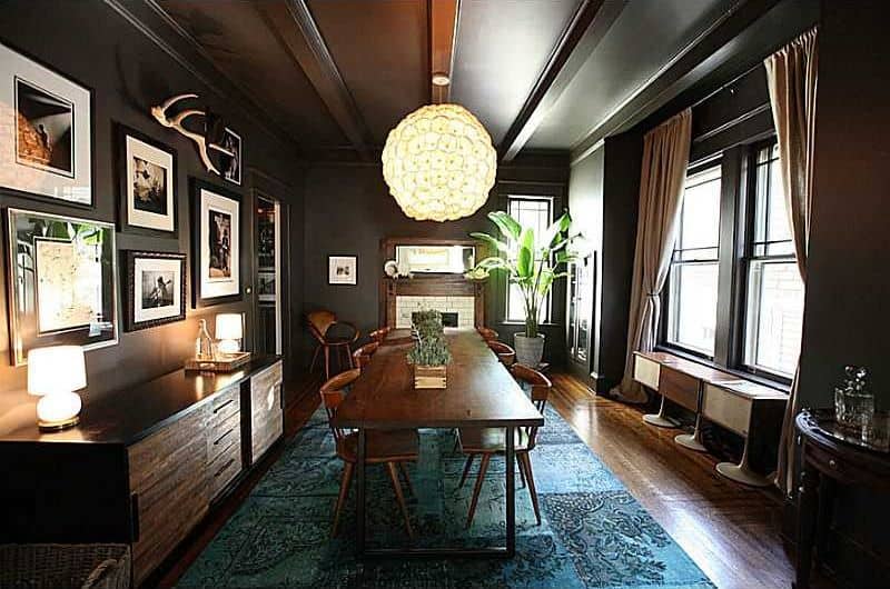 Black craftsman dining room designed with gallery frames mounted above the buffet table. It has a 6-seater dining set illuminated by a charming chandelier.