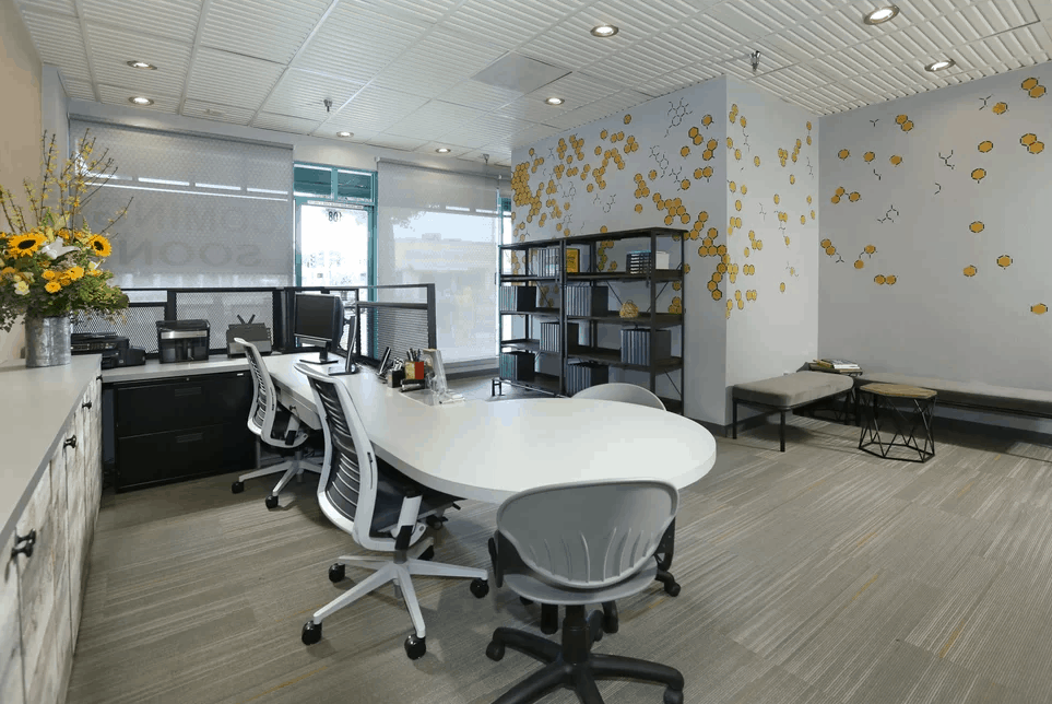 Contemporary home office with a white desk surrounded by modern office chairs. It includes steel open shelving units and a spacious seating area in the corner.