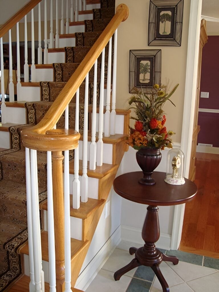 The foyer has a wooden staircase and a round wooden table adorned with a flower vase.