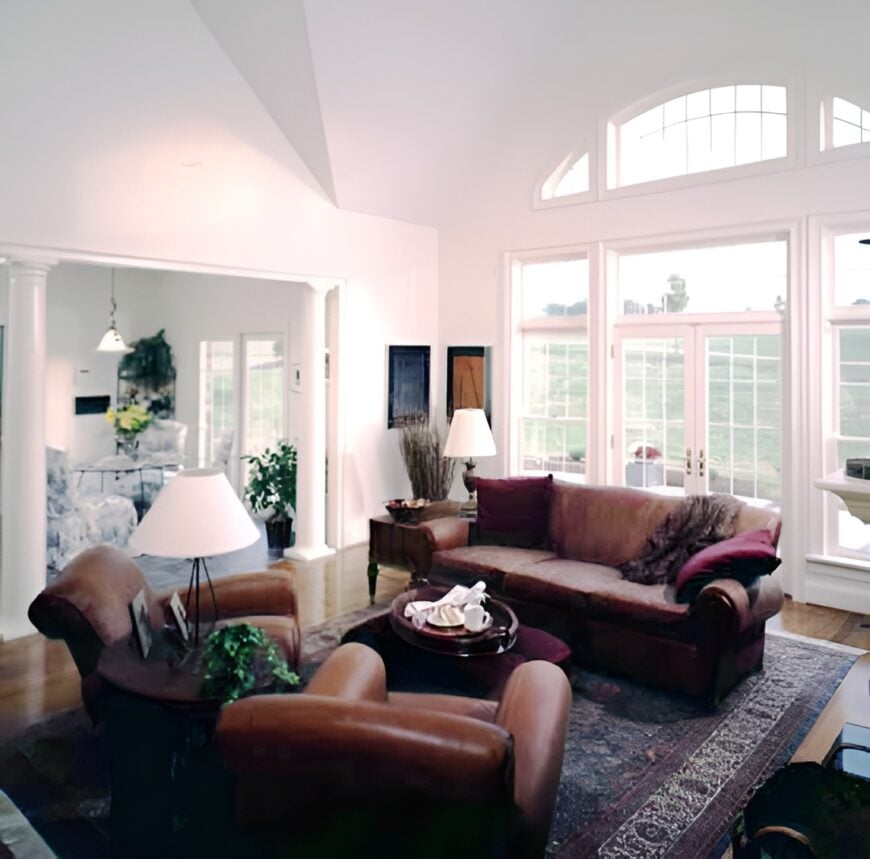 The family room has brown leather seats and a wall of windows that bring ample natural light in.