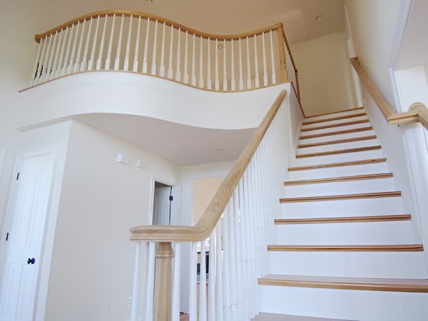 Staircase and balcony with white risers and spindles accentuated with light wood treads and railings.