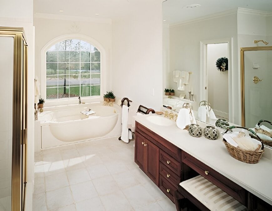 Primary bathroom with a dual sink vanity, a walk-in shower, and a drop-in bathtub fixed under the arched window.