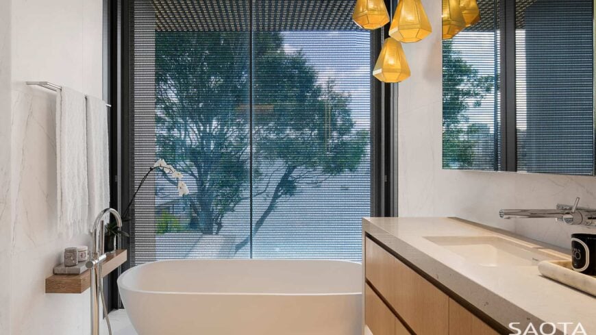 Contemporary primary bathroom with pedestal tub and a wooden floating shelf along with a single sink vanity topped with smooth marble countertop.
