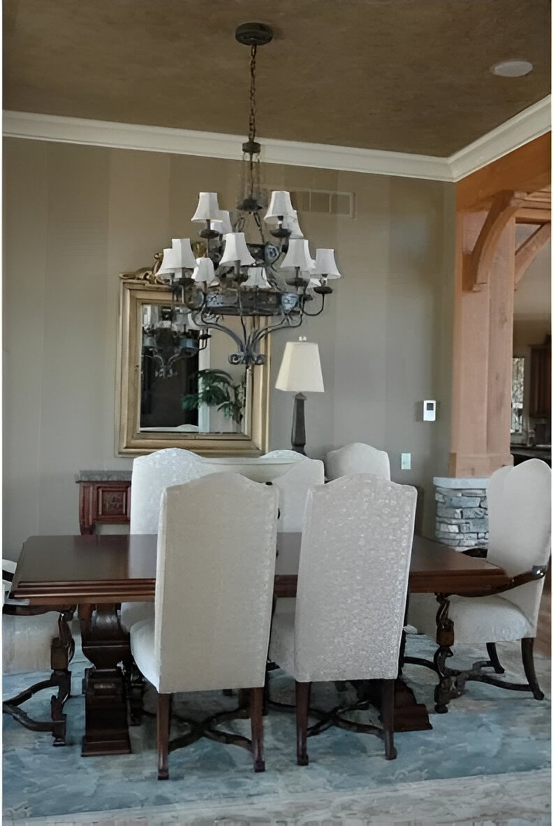 Formal dining room with gray high back chairs and a dark wood dining table topped with an ornate wrought iron chandelier.