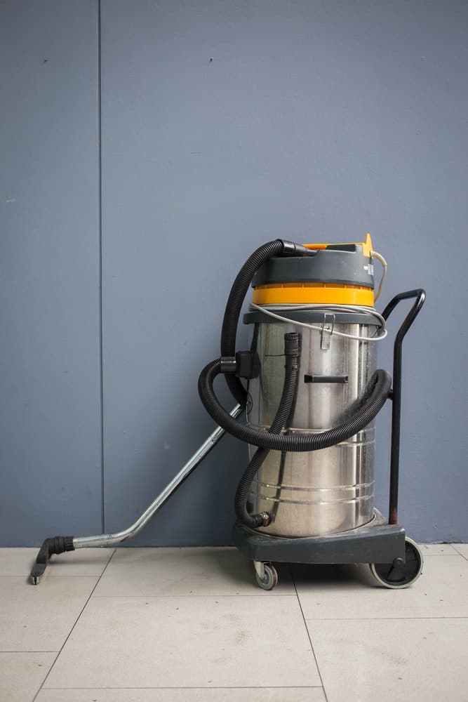 Vacuum cleaner with wheels standing on tile flooring.
