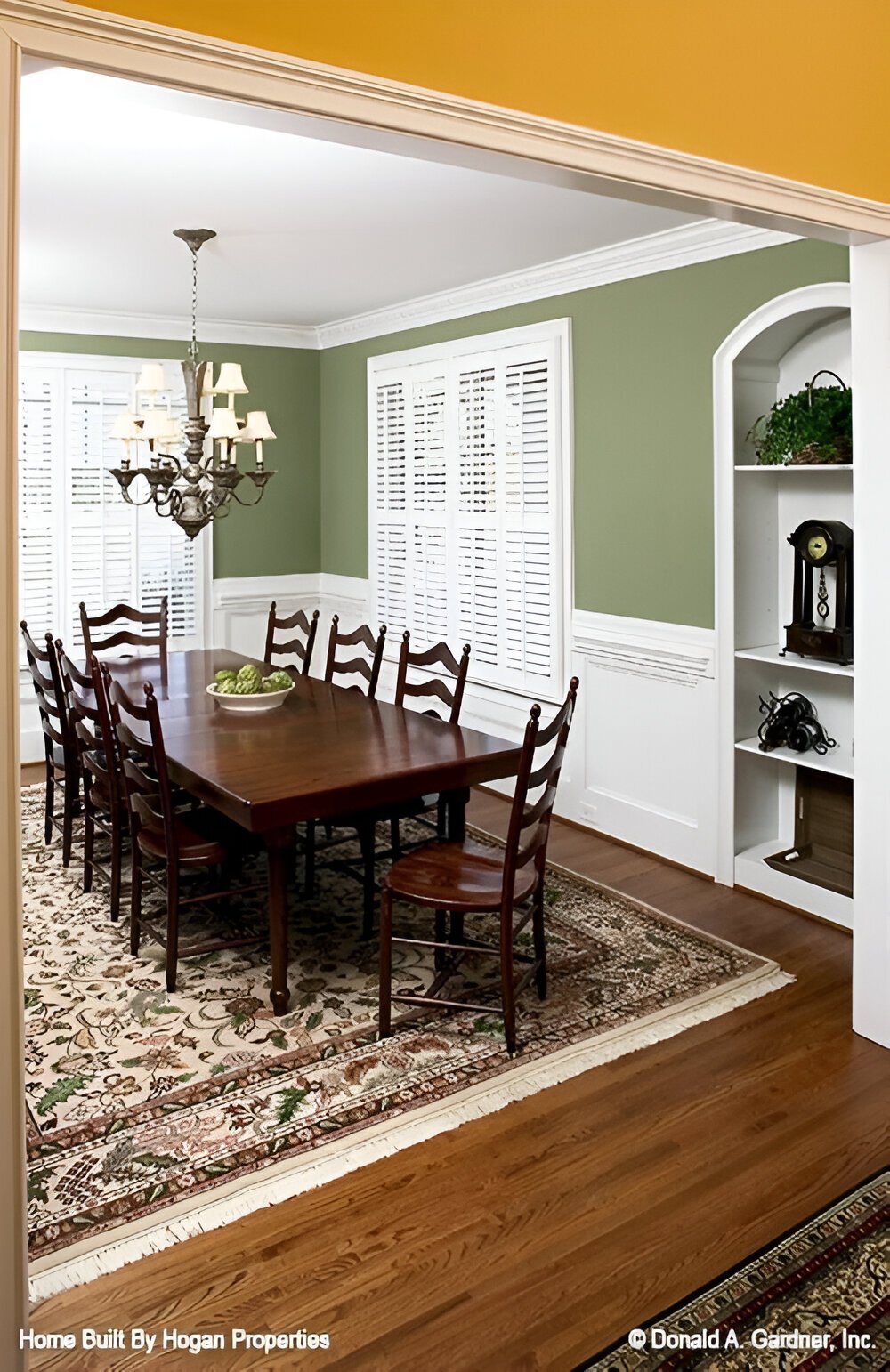 Formal dining room with an 8-seater dining set, built-in shelves, and green walls graced with white wainscoting.