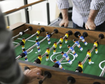 Two people playing foosball, one in the yellow team and the other in the blue team.