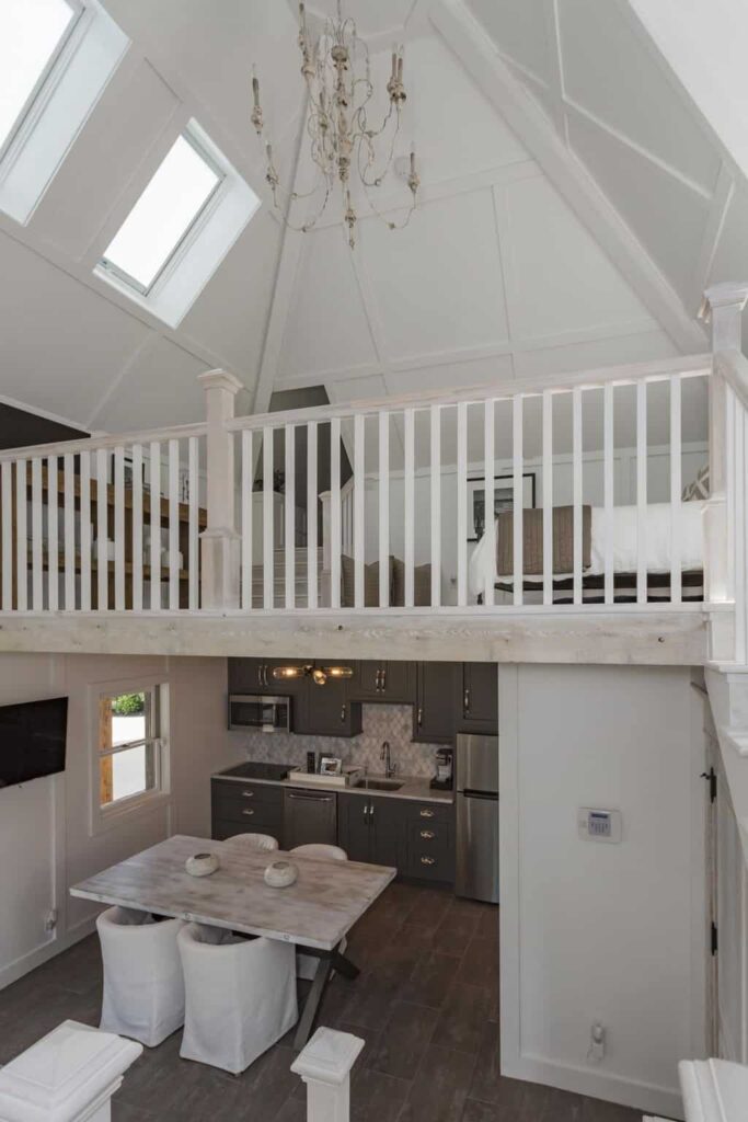 A dine-in kitchen situated under the loft bedroom featuring gray cabinetry and wooden dining table with white round back chairs.