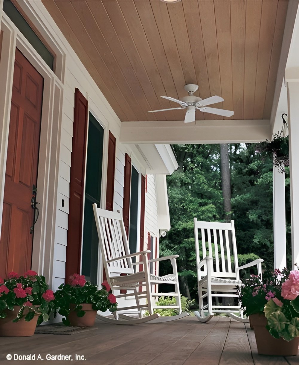 Covered front porch with white rockers, potted plants, and a white ceiling fan mounted on the wood-paneled ceiling.Covered front porch with white rockers, potted plants, and a white ceiling fan mounted on the wood-paneled ceiling.