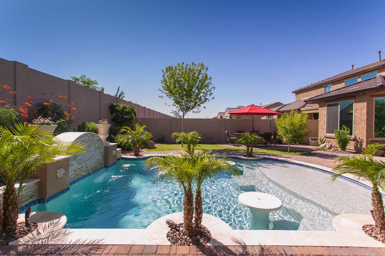 Desert suburban home with a tiny backyard pool with a lounge ledge. See the shallow area? That's a lounge edge where you can place lounge furniture. I love that. Notice the table in the pool as well. This is purely for cooling off... can't really do laps.