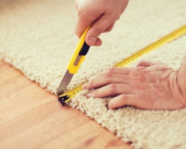 A man is using a utility knife to cut a portion of the carpet.