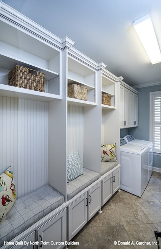 Laundry room with top-load appliances, white cabinets, and built-in seats topped with gray cushions and patterned pillows.