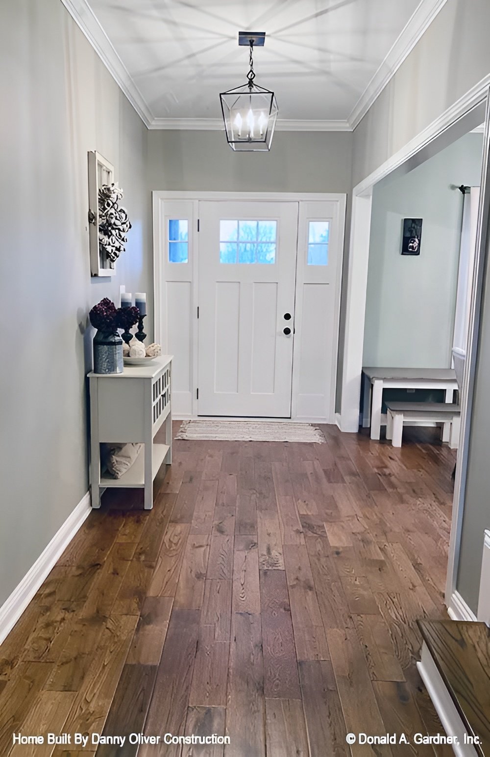 The foyer has a white entry door, caged pendant, and a white console table topped with a flower vase and candles.