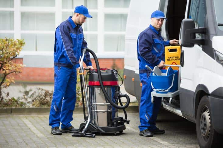 Two house cleaners unloading cleaning equipment from van