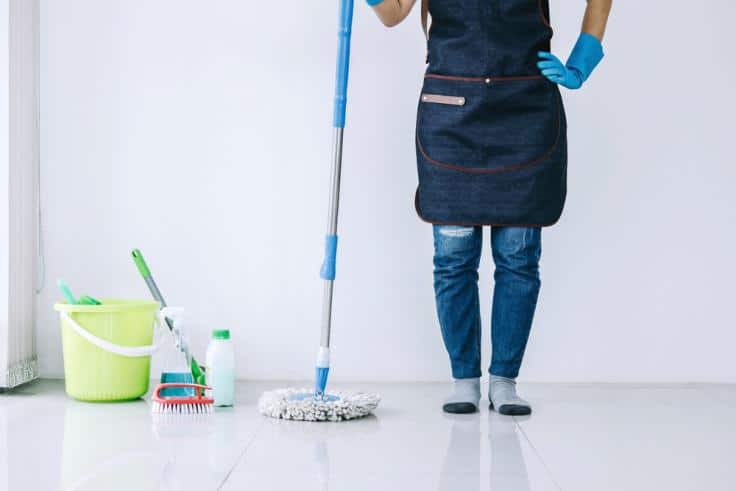 House cleaner wearing apron standing with mop on a reflective floor