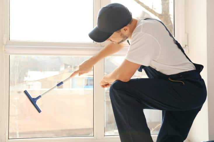 House cleaner wearing a black cap wiping the window from the inside