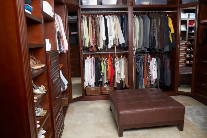 Luxury walk-in closet with drawers, shoe storage, side mirrors, and an ottoman.