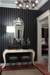 This cool glam black and white foyer features beautiful hardwood floors adorned with a jute rug, and black striped wallpaper which brings depth to the space.