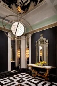 This elegant black foyer features a gorgeous tile pattern flooring and unique ceiling light. Gilded console table with antique mirror hanging above contrasts against the black walls and white trim.