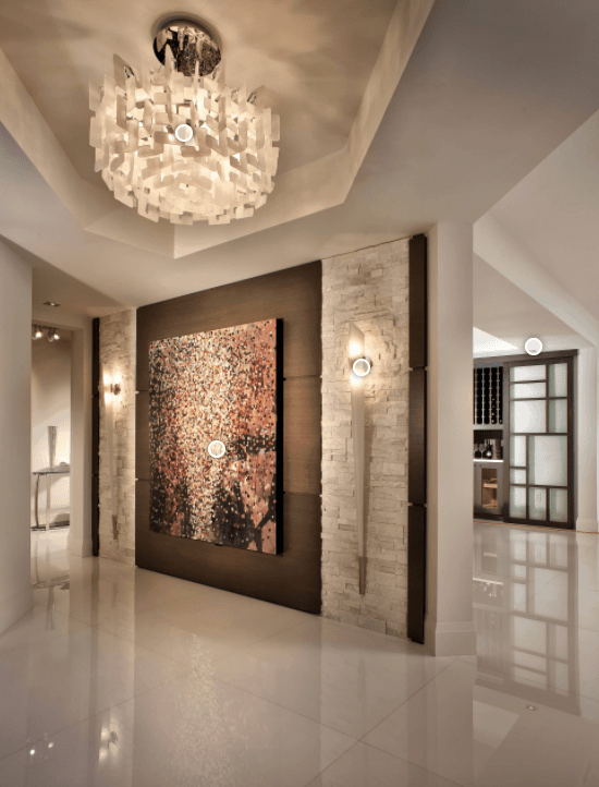 Fabulous foyer illuminated by a gorgeous chandelier that hung from a tray ceiling. It is designed with a huge canvas painting mounted on a wooden wall that's accented with bricks and vertical sconces.