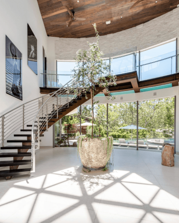 Contemporary foyer with a huge potted plant beside the curved staircase. It has a floor to ceiling windows and white tiled flooring.