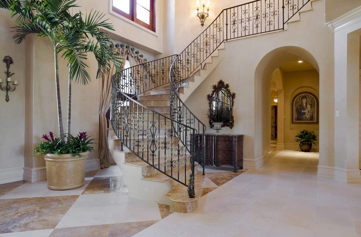A large foyer featuring classy tiles flooring and staircase. The wall lighting looks so beautiful while the indoor plants add beauty to the home's entry.