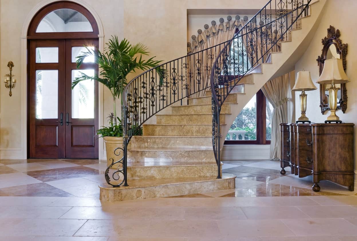 This large foyer boasts a stunning staircase featuring marble steps with iron railings. The curtains are also very beautiful.