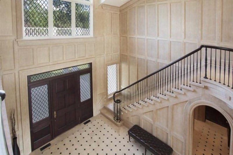 Top view of a large foyer featuring white walls and flooring and a large door. The staircase looks classy.
