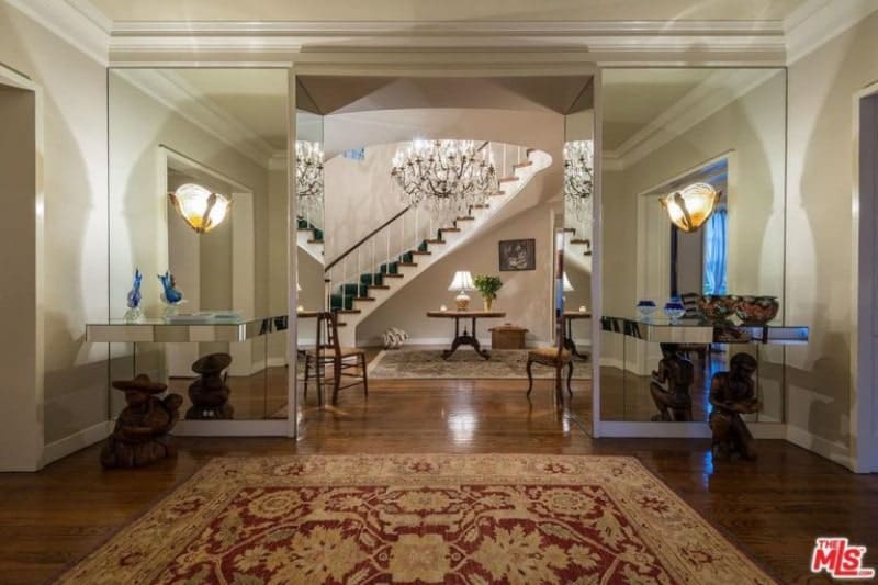 This modish large foyer features elegant hardwood flooring topped by a rug. The glass mirrors are very charming along with the grand chandelier.