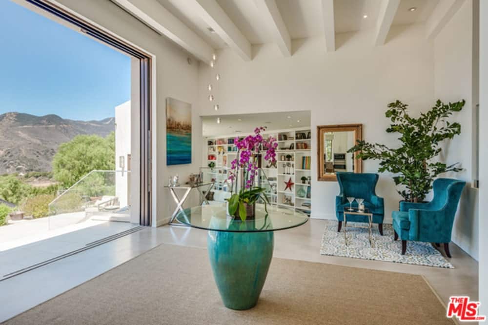 Modish large foyer with white walls and ceiling along with the flooring topped by rugs.