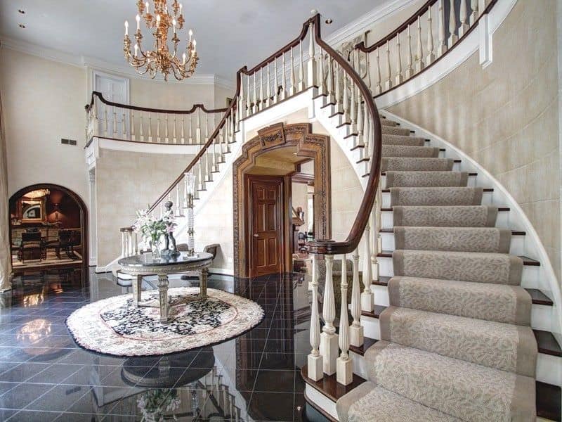 This large foyer features a dark tiles flooring along with light colored walls. The staircase and the chandelier are absolutely stunning.