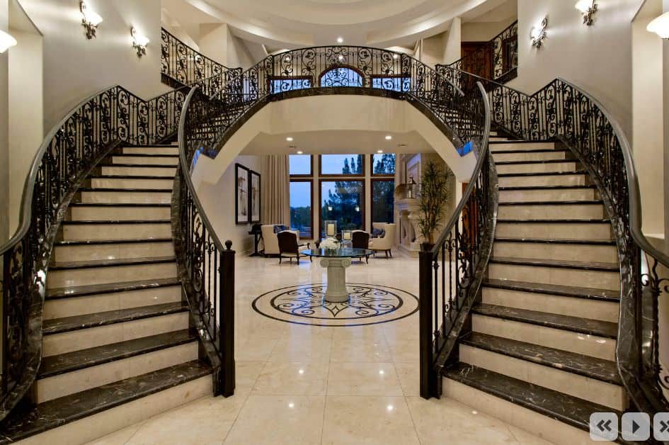 A very elegant large foyer featuring gorgeous flooring, staircases and lighting.